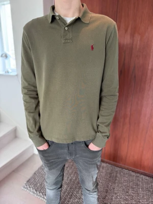 Olivgrön långärmad piké från Polo Ralph Lauren - Säljer en klassisk långärmad pikétröja från Polo Ralph Lauren i en snygg olivgrön färg med röd logga. Väldigt fint skick och sitter riktigt bra tack vare Slim Fit-passformen. • Märke: Polo Ralph Lauren • Storlek: Large men passar Medium (Slim Fit) • Skick: Mycket bra •Färg: olivgrön.      •Nypris: ca 1500kr