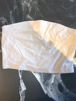 Beige bandeau tubtopp från 157 - Säljer en enkel och stilren beige bandeau tubtopp från 157. Toppen är axelbandslös och har en mjuk, stretchig känsla som gör den bekväm att bära. Perfekt att matcha med höga jeans eller kjol för en clean look.