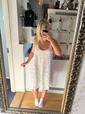 Vit spetsklänning med tunna band - Säljer en superfin vit klänning med tunna axelband och vackert spetsmönster över hela plagget. Banden går snett över ryggen