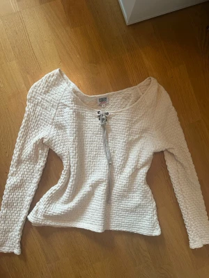 Vit långärmad topp med snörning - Säljer en vit långärmad topp från country line med snygg snörning framtill. Perfekt att styla med jeans eller kjol för en cool outfit. Passar nästan som storlek S