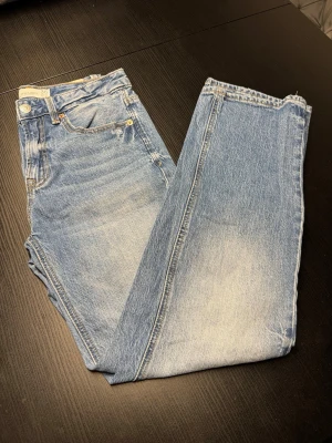 Blå raka jeans från Stradivarius - Säljer ett par ljusblå raka jeans från Stradivarius med klassisk femficksmodell och hög/medelhög midja. Jeansen har en snygg tvättad look med ljusa partier och raka ben. Tillverkade i bomull för en skön och avslappnad stil.