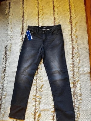 Grå slim fit jeans från Jack & Jones - Snygga grå slim fit jeans från Jack & Jones med klassisk femficksdesign och svarta sömmar. Jeansen har en modern tvättad look och är tillverkade i stretchigt material för extra komfort. Perfekta för dig som vill ha en stilren och trendig vardagslook.