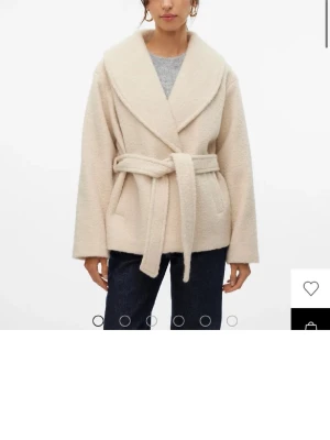 Beige kappa med knytskärp - Stilren beige kappa med bred sjalkrage och knytskärp i midjan och är ifrån veromoda. Kappan har en mjuk, ull-liknande struktur och raka ärmar. Jätte snygg kappa som passa både våren, hösten och vintern. Den är väldigt fluffig och skön. Aldrig använd 