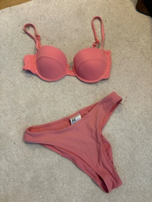 Rosa ribbad bikini från H&M - Snygg rosa bikini från H&M med ribbad struktur. Överdelen har bygel och reglerbara axelband för extra stöd och passform. Underdelen är klassisk med hög benskärning. 
