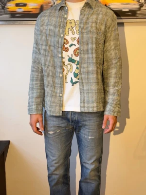 Grön Flanell  - Snygg grönrutig skjorta med klassisk krage och knappar framtill. Skjortan är tillverkad i mjuk bomull och har en avslappnad passform. Perfekt att bära öppen över en t-shirt för en casual look.