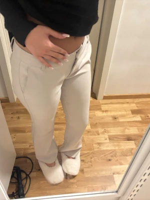 Beiga kostymbyxor med raka ben - Säljer ett par stilrena beiga kostymbyxor med raka ben och hög midja. Byxorna har diskreta fickor i sidorna och stängs med knapp och dragkedja. Perfekta för en clean och modern look. Materialet känns mjukt och följsamt.
