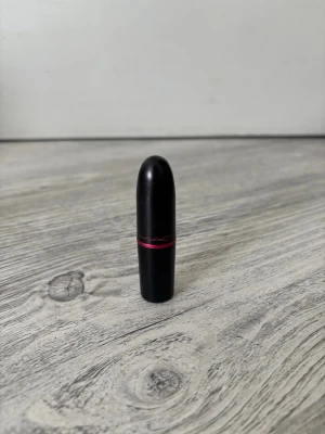 MAC nude läppstift med röd detalj - Snyggt nude-färgat läppstift från MAC i klassisk svart hylsa med röd detalj. Läppstiftet har en mjuk, krämig formula och kommer i en stilren, rundad förpackning som är enkel att ta med i väskan. Perfekt för dig som gillar naturliga toner på läpparna.