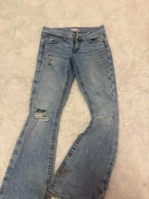 Ljusa slitna jeans från Gina Tricot - Säljer ett par låg midjade ljusblå jeans från Gina Tricot med trendiga slitningar på benen och klassisk femficksmodell. Är tillverkade i ett mjukt denimtyg. 🌹💕