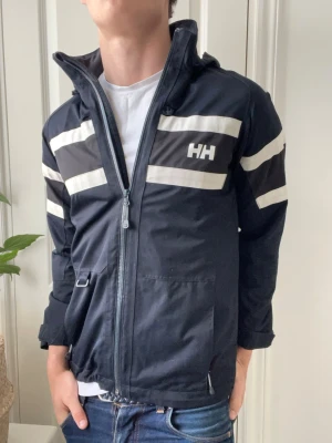 Helly Hansen vindjacka - Helly Hansen vindjacka, inga defekter. Storlek 14 vilket motsvarar i helly Hansen storlekar S i vanlig. Helly Hansen brukar vara större i storleken. Modellen som bär den är 180 cm 75 kg och jackan är för liten på honom. Kom med frågor! 