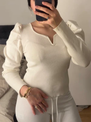 Vit ribbad topp med puffärm från BIK BOK - Säljer en vit ribbad topp från BIK BOK med långa puffärmar och en snygg v-ringad detalj framtill. Toppen är figurnära och har en mjuk, stretchig känsla som gör den superbekväm. Perfekt att styla med både jeans och kjol.