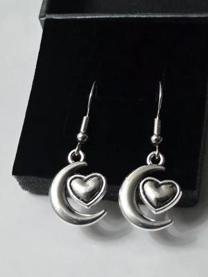 Silver Moon & Heart Örhängen – Rostfritt stål ✨ - Handgjorda örhängen med en himmelsk kombination av måne och hjärta. Eftersom de är gjorda i rostfritt stål håller de sig fina över tid utan att mörkna. Perfekta för dig som vill ha en magisk look som tål att bäras varje dag! ​Detaljer: ​Material: Rostfritt stål (slitstarkt & nickelsäkert) ​Längd: 25 mm ​Bredd: 15 mm ​Skick: Helt nya / Egendesignade