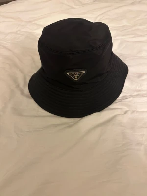 Prada hat - Tja, säljer en helt ny svart Prada hat som aldrig har vart använd, den förekommer även med tagen som man ser på bilden. Den är perfekt för sommaren eller om man bara vill ha en fräsch look. Hör av dig vid vidare frågor.