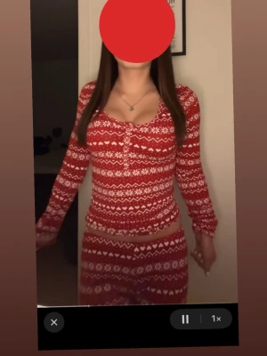 Röd julpyjamas med mönster - Supermysig röd pyjamas med vitt juligt mönster. Setet består av långärmad tröja med knappar framtill och matchande byxor med resår i midjan. Perfekt för vinterkvällar och julmys. Materialet ser ut att vara mjukt och stretchigt, troligen bomull eller bomullsblandning.