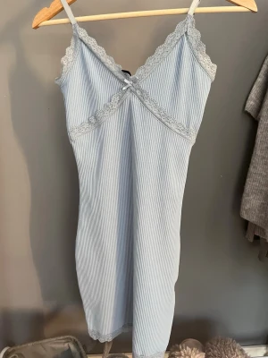 Ljusblå ribbad kortklänning med spets - Söt ljusblå kortklänning med smala axelband och ribbad struktur. Klänningen har spetsdetaljer längs urringningen och ärmlös design. Perfekt för varma dagar och enkel att styla med accessoarer.