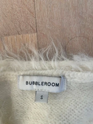 Vit fluffig omlottkofta Bubbleroom - Supersöt vit stickad omlottkofta från Bubbleroom i fluffigt material. Koftan har långa ärmar, ribbade muddar och knyts i midjan för en snygg siluett. Perfekt för lager på lager och ger en mysig vibe till din outfit.