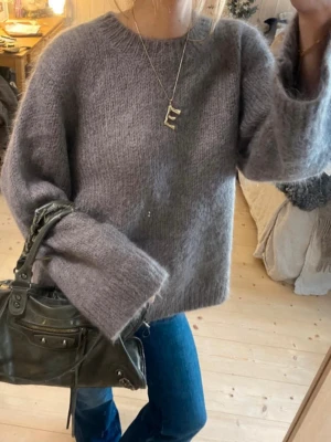 Grå fluffig stickad tröja - Mysig stickad tröja med oversized passform och breda ärmar. Tröjan har rund halsringning och är gjord i ett fluffigt material som ger en trendig look. Perfekt att matcha med jeans för en avslappnad stil.