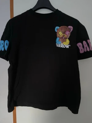 Svart Barrow t-shirt med nalletryck -  svart t-shirt från Barrow med färgglatt nalletryck fram och stort tryck på ryggen. Texten 'I JUST WANT TO FEEL GOOD' på baksidan och Barrow-logga på ärmarna i blått och rosa. 