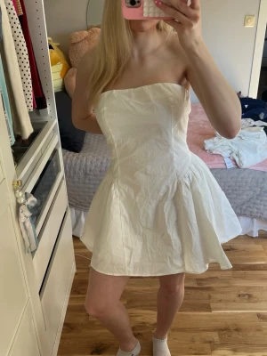 Vit axelbandslös kort klänning - Säljer en söt vit axelbandslös klänning med utsvängd kjol och figurnära passform. Helt ny med prislapp från boohoo, endast testad! Storlek L men passar en M💕