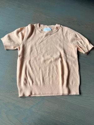 Ljusrosa stickad topp från Arket - Supersöt ljusrosa stickad topp från Arket med rund halsringning och korta ärmar. Mjuk och skön kvalitet som passar perfekt till jeans eller kjol. Enkel och stilren design med ribbade kanter nedtill och vid ärmsluten.