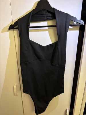 Svart halterneck body - Snygg svart body med halterneck och djup urringning. Tillverkad i stretchigt tyg som formar sig efter kroppen. Den är i nytt skick utan prislapp på.