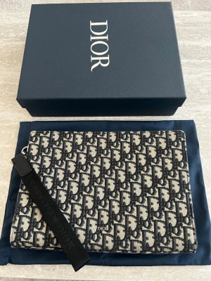 DlOR NAVY BLUE POUCH - Säljer denna klassiska väska i det ikoniska Oblique-mönstret. Väskan är både stilren och praktisk,  Detaljer: Modell: Oblique Canvas Clutch (Navy Blue/Beige) Skick: Ny skick (se bilder för detaljer).  Tillbehör: Kommer med originalbox, dustbag och veriferingskort. En tidlös accessoar som aldrig går ur tiden. Passa på att fynda en lyxig klassiker!  Skickas spårbart och försäkrat. Tveka inte att skicka ett meddelande om du har frågor eller vill ha fler bilder!