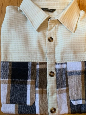 Rutig skjorta från ChicMe XL - Snygg skjorta från ChicMe i storlek XL. Överdelen är ljusbeige med diskreta ränder och nederdelen har ett rutigt mönster i svart, beige och vitt. Skjortan har klassisk krage, stora knappar och två bröstfickor. Perfekt för en trendig och avslappnad stil.