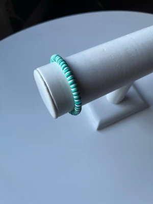 Grönt och vitt armband  -  Ett grönt och vitt armband som har elastiskt band och även ett guldlås så man kan knäppa det också. Armbandet är handgjort.