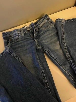 Blå jeans från Gina tricot storlek 152 - Säljer ett par blåa jeans ifrån Gina tricot. Har en del slitningar på framsidan för design och broderade bakfickor. Använda väldigt få gånger och är i väldigt bra skick. Passar för en mer kortare person. Säljer då de inte gått till användningen. Storlek 152