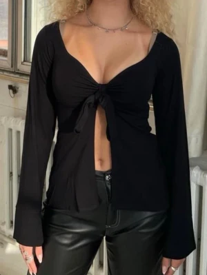 Svart långärmad topp med knyt - Trendig svart långärmad topp med djup v-ringning och knyt framtill. Toppen har en croppad passform och vida ärmar som ger en cool look. Perfekt att styla med höga byxor eller kjol för en edgy outfit. Använd men inget slitage 🥰🤩
