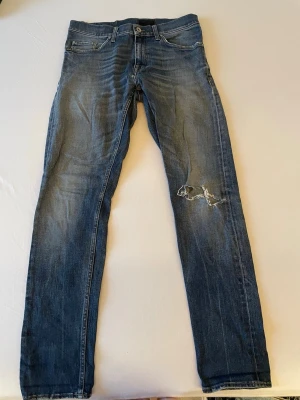  Jeans från Tiger of Sweden med hål på knät - Säljer ett par blå jeans i slim fit-modell med slitningar och ett hål på höger knä. Klassisk femficksdesign och normal midja. Modellen är Pistolero. Nypris 1600.