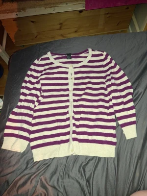 Lila och vitrandig kofta H&M - Snygg kofta från H&M med lila och vita horisontella ränder. Koftan har rund halsringning, knäppning framtill med vita knappar och långa ärmar. Perfekt att slänga över en t-shirt för en chill look.