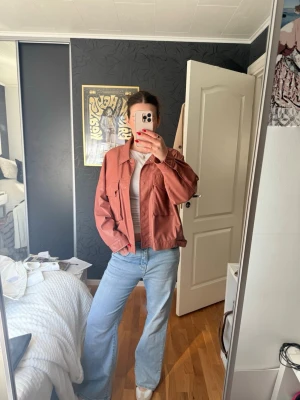 Rostbrun skinnjacka med fickor - Säljer en roströd/rosa skinnjacka i oversized modell med stora bröstfickor och klassisk krage. Jackan har knappstängning framtill och raka ärmar!