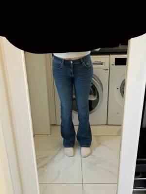 Blå bootcut jeans från Gina Tricot - Säljer ett par blå bootcut jeans från Gina Tricot med klassisk femficksmodell och normalhög midja. Jeansen har en snygg tvätt och lätt utsvängda ben som ger en trendig siluett. Perfekta till sneakers eller boots för en cool vardagslook.
