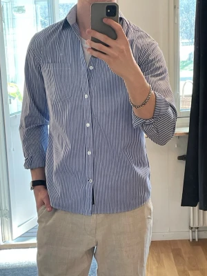Blårandig skjorta med knappar - Snygg blårandig skjorta med klassisk krage och vita knappar. Skjortan har lång ärm och är tillverkad i ett lätt bomullstyg som passar perfekt till både jeans och chinos. Enkel och stilren design som funkar till många olika looks. Perfekt till sommaren ☀️