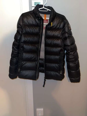 Svart dunjacka Parajumpers Sheen - Snygg svart dunjacka från Parajumpers, modell Sheen. Jackan har quiltad design, hög krage och dragkedja framtill. Insidan är ljusgrå och jackan har två fickor med dragkedja. Perfekt för kalla dagar och riktigt stilren look.