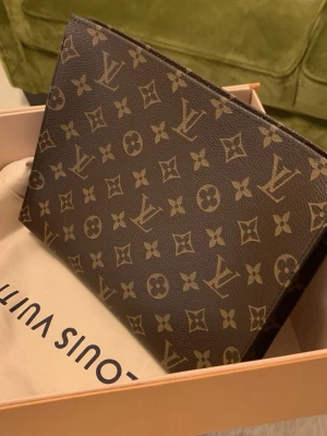 Louis Vuitton clutch - Säljer en klassisk brun clutch från Louis Vuitton med det ikoniska monogrammönstret i beige. Box, dustbag och kvitto medföljer. Nypris: 11000