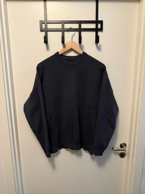 Mörkgrå stickad tröja unisex - En enkel och stilren mörkblå stickad tröja med rund halsringning och ribbade muddar vid ärmslut och nederkant. Perfekt för lager på lager och passar till det mesta. Oversized fit för en avslappnad look.