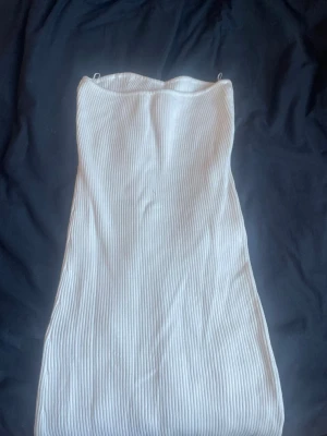 Vit ribbad axelbandslös klänning - Säljer en vit ribbad klänning med slits och axelbandslös design. Klänningen har en kroppsnära passform och är perfekt för sommarens alla tillfällen. Materialet är mjukt och stretchigt, vilket gör den både bekväm och snygg (klicka ej köp nu) kontakta gärna och Swish går jätte bra ❤️❤️.