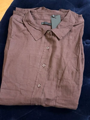 Brun linneskjorta med knappar - Snygg brun skjorta i linne med klassisk krage och knäppning framtill. Skjortan har en bröstficka och en avslappnad passform, perfekt för en stilren look. Passar till både jeans och chinos.