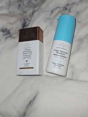 Drunk Elephant D-Bronzi & F-Balm duo - Säljer två produkter från Drunk Elephant: D-Bronzi Anti-Pollution Sunshine Drops i brun/vit förpackning och F-Balm Electrolyte Waterfacial i vit/blå förpackning. Perfekt för dig som vill boosta huden med bronzing drops och återfuktande water cream