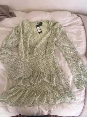 Grön blommig omlottklänning - Säljer den här jätte fina volang klänningen från Prettylittlething, då den tyvärr inte passar mig. Helt oanvänd med prislapp kvar.