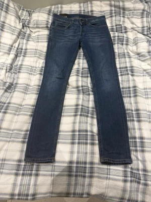 Blå dondup slim fit jeans med stretch - Säljer ett par blå dondup slim fit jeans med lätt tvättad look och klassisk femficksmodell. Jeansen har smal passform och är tillverkade i ett stretchigt denimtyg för extra komfort. Perfekta för dig som gillar en modern och enkel stil.