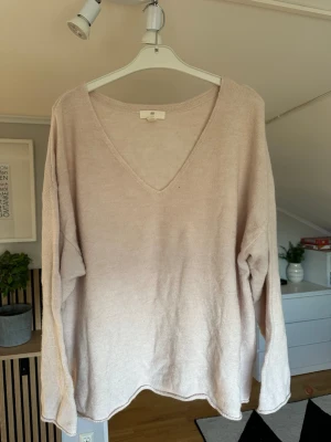 Ljusrosa stickad tröja från H&M - Mysig ljusrosa stickad tröja från H&M med djup V-ringning och avslappnad passform. Tröjan har långa ärmar och är tillverkad i ett mjukt material som känns skönt mot huden. Perfekt för lager på lager och enkel att styla.