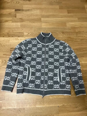 Gucci Grå ziptröja  - Säljer en grå stickad ziptröja från Gucci med vitt GG-mönster över hela tröjan. Den är ny har inga skador den är strl S pris kan diskuteras och tar byten beror på vad det är.