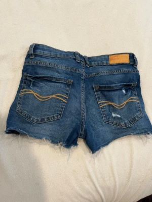 Blå lågmidjade jeansshorts med snygg design på fikorna - Säljer ett par blå lågmidjade jeansshorts med fina detaljer, Bakfickorna har dekorativa sömmar. De är perfekta till sommaren eller varmare väder.
