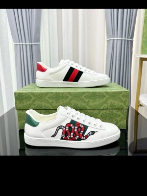 Gucci vita sneakers med orm och ränder - Säljer ett par vita Gucci sneakers i läder med gröna och röda detaljer. Ena skon har en broderad orm i rött, svart och vitt, medan den andra har klassiska gröna och röda sidoremsor. Skorna har lågt skaft och vita snören. Helt nya 