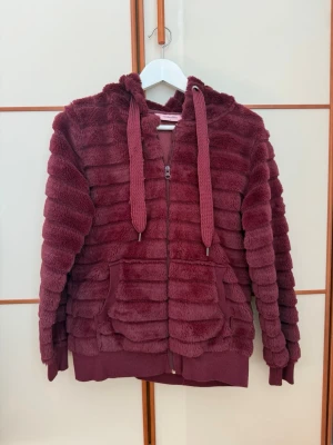 Vinröd hoodie - Cool vinröd zip up hoodie från hunkemöller i storlek S. Den är lite oversized så skulle nog även passa storlek M. Knappt använd så i väldigt fint skick, bortsett från snörerna som är lite tilltufsade. Supermjuk och härlig, passar perfekt nu till våren.