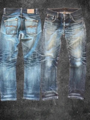 Blå slitna jeans från Nudie Jeans - Säljer ett par blå jeans från Nudie Jeans med tydliga slitningar och tvättade detaljer. Jeansen har raka ben, klassiska fem fickor och kontrastsömmar. Materialet är denim i bomull och passformen är normal. Perfekta för en avslappnad streetstil.