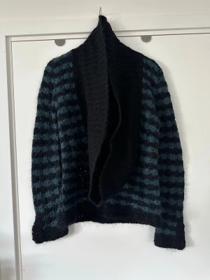 By Malene Birger - stickad blå svart kofta, 100% ull - storlek M - Svart och blårandig mönsterstickad kofta från By Malene Birger i storlek M med en öppen design och en bred krage. Koftan har långa ärmar och ett mönster av horisontella ränder i svart och blått. 100% ull, så bra material som andas. Nypris 2995:-. Mycket gott skick, som ny!