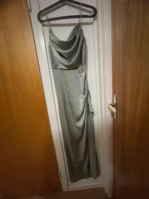 Lång ljus grön färgad klänning med drapering - Elegant långklänning satin med tunna axelband och snygg drapering över bysten. Klänningen har en figurnära passform och ett släp som ger extra effekt. Perfekt för dig som vill sticka ut på bal eller fest.